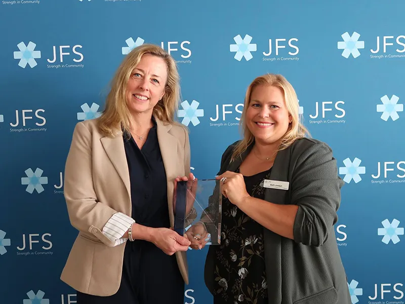 Two women standing in front of wall with JFS logos